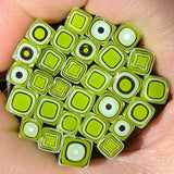 A close-up image of a hand holding a collection of small, square-shaped objects with a green and black color scheme.