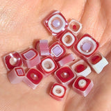 A hand holding a collection of small, colorful beads in shades of red and white.