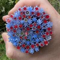 A hand holding a large collection of colorful flower-shaped objects, including red and blue flowers, against a natural background.