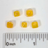 a collection of yellow beads, each with a unique shape, arranged on a white surface next to a ruler for size comparison.