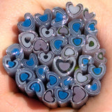 A hand holding a collection of heart-shaped objects made of glass or plastic, with various colors and patterns.