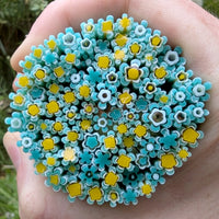 A hand holding a circular arrangement of small, colorful flower-shaped objects in shades of blue and yellow.