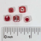 a collection of red and clear beads, with a ruler for scale placed below them.